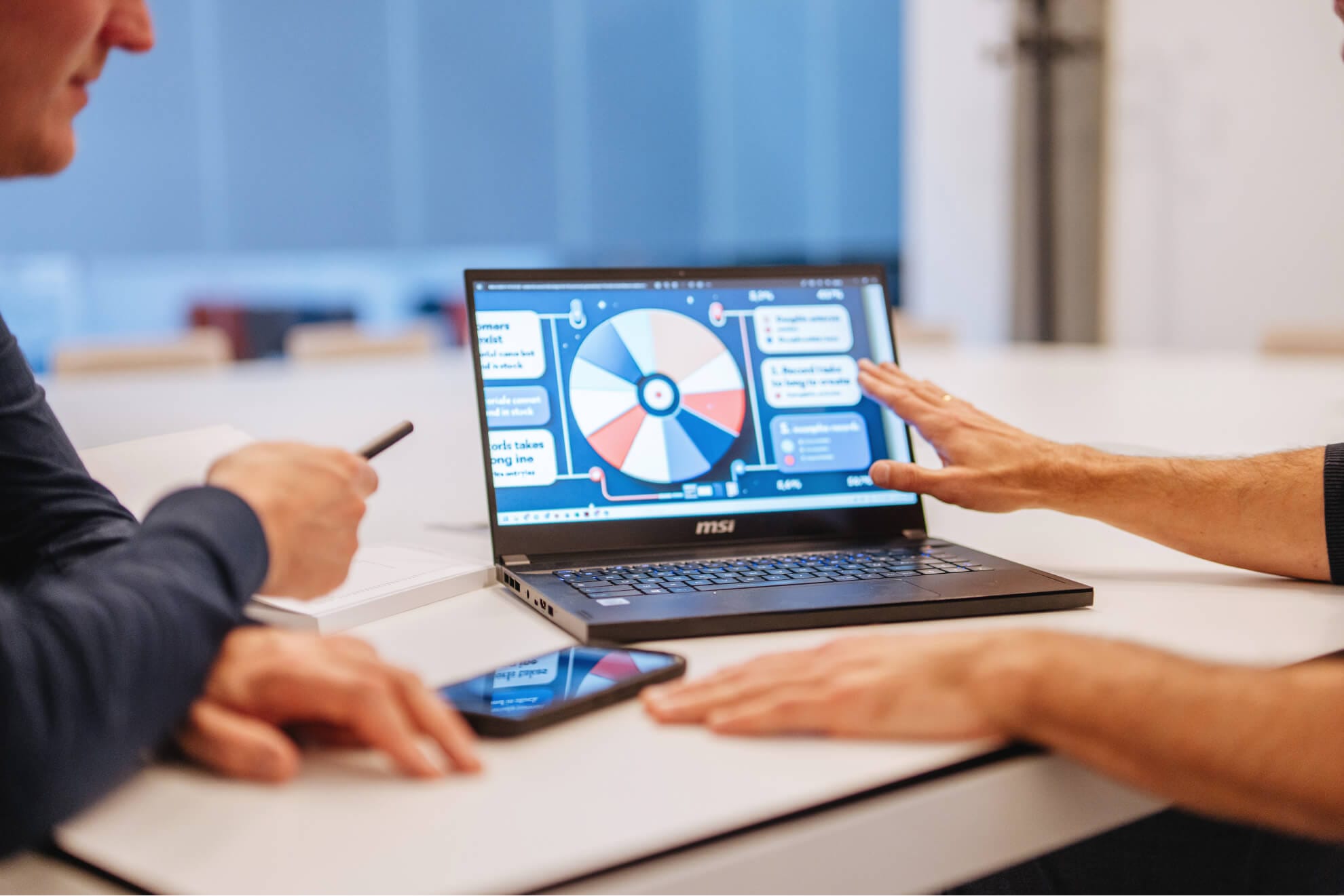 Two men looking at a laptop with a pie chart on it.